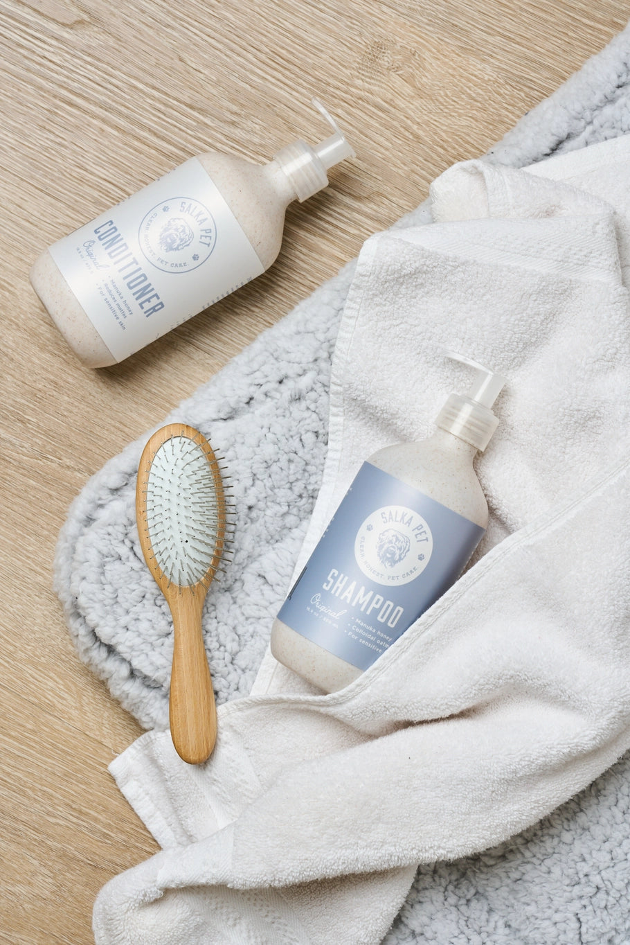 Two bottles of shampoo, a wooden brush, and a towel on a wooden surface.